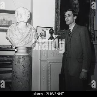 1960s, historique, Merlin Charles Sainthill Hanbury-Tracy, 7th Baron Sudeley, le Seigneur Sudeley debout à côté d'un buste en marbre de son ancêtre, Charles Hanbury-Tracy, 4th Baron Sudeley. L'honorable 4th Baron, un politisé libéral, était célèbre pour son manoir gothique, Toddington Manor, qui serait en partie un modèle pour les chambres du Parlement lorsqu'elles ont été construites en 1840s après un incendie. Banque D'Images