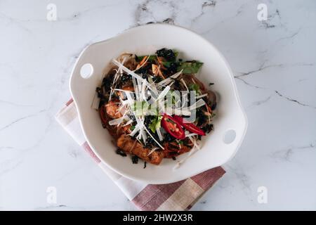 Saladier japonais coréen poêlé avec nouilles aux chapchae, bœuf et légumes isolés sur le dessus du tapis, sur fond de marbre gris Banque D'Images