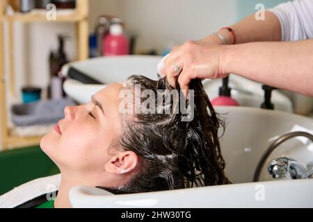 Coiffeur lave la tête d'une fille de brunette avec du shampooing dans le salon de beauté Banque D'Images