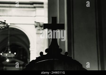 Croix religieuse en bois sur un confessionnel dans l'intérieur sombre d'une église catholique, avec un fond hors foyer, noir et blanc. Banque D'Images