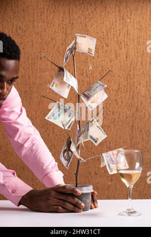 Plan vertical d'un jeune homme d'affaires africain observant un arbre de l'argent Banque D'Images