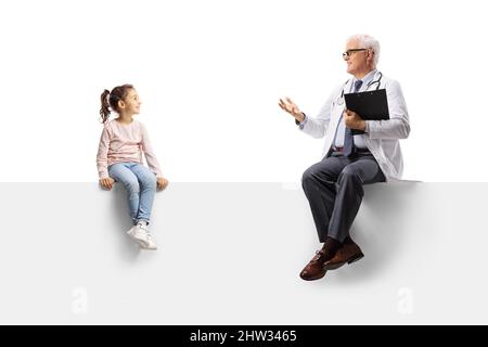 Médecin assis sur un panneau vierge et parlant à une petite fille isolarée sur fond blanc Banque D'Images