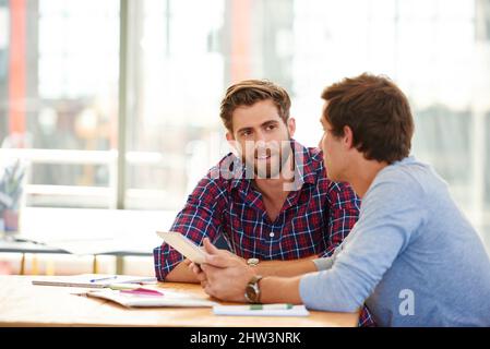 En parlant de leurs plans. Prise de vue de deux collègues utilisant une tablette numérique dans un bureau. Banque D'Images