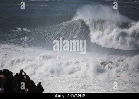 João Guedes à cheval sur une vague géante sur la plage nord de Nazaré, au Portugal, tandis que les spectateurs regardent en incrédulité. Banque D'Images