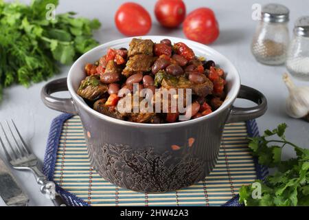 Lobio de viande de bœuf, haricots rouges, oignons, ail, épices et tomates dans un plat en céramique sur fond gris. Cuisine géorgienne Banque D'Images