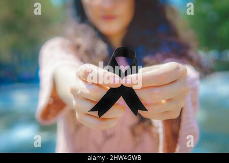 Une femme porte un ruban de sensibilisation. Ruban noir pour la sensibilisation au cancer du mélanome. Banque D'Images