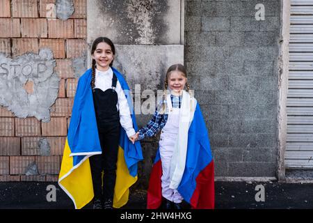 Petites filles avec des drapeaux ukrainiens et russes devant un mur détruit par des bombes. Ukraine russie conflit 2022 escalade. Concept de paix Banque D'Images