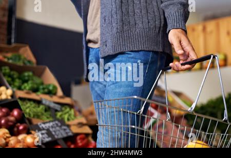 Choisissez les plus frais. Coupe courte d'un jeune homme qui descend dans une allée d'épicerie et qui porte un panier contenant de la nourriture. Banque D'Images