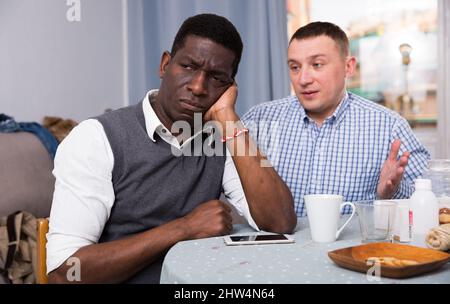 Deux tristes hommes interraciaux assis à la table après le conflit Banque D'Images
