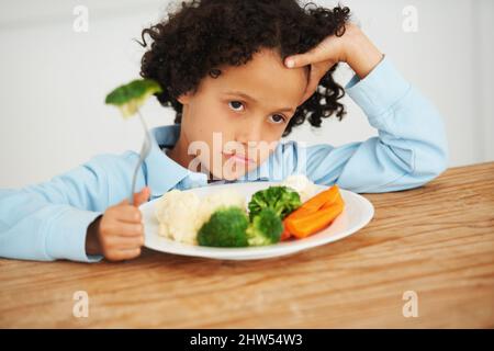 Brocoli à nouveau. Photo d'un petit garçon à l'aspect peu impressionné assis devant une assiette de légumes. Banque D'Images