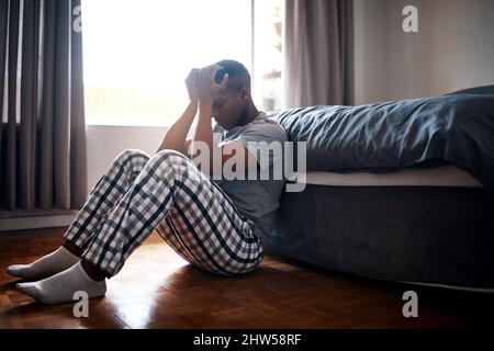 Pourquoi suis-je si déprimé. Plein cliché d'un jeune homme beau assis au pied de son lit et se sentant déprimé à la maison. Banque D'Images