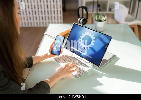 Femme effectuant la mise à jour de logiciels sur un téléphone mobile et un ordinateur portable Banque D'Images