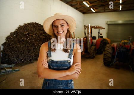 Agricultrice caucasienne debout dans un hangar avec les bras croisés portant un chapeau de cow-boy Banque D'Images