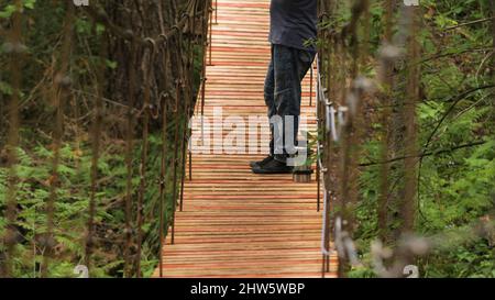 Le voyageur bénéficie d'une vue sur le pont suspendu. Films. L'homme s'est arrêté sur un pont en bois pour admirer la beauté de la nature. Homme fumant tuyau wh Banque D'Images