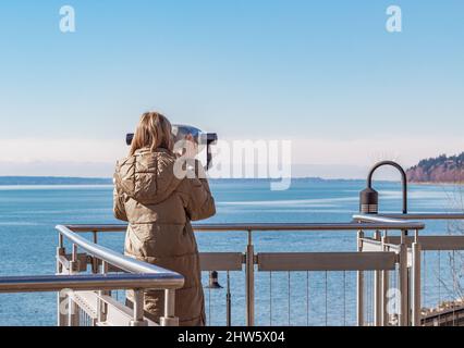 Jeune belle femme sur Un quai près de la mer regarde à travers les jumelles sur. Recherche de voyage concept de voyage Banque D'Images