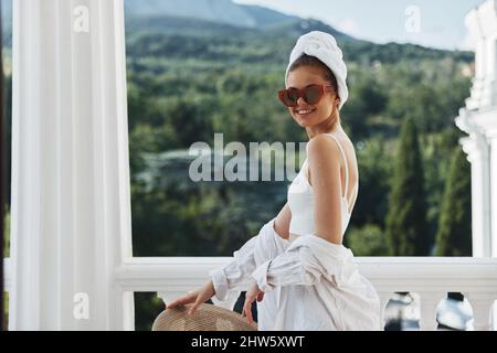 une femme gaie avec une serviette sur la tête en verres foncés se tient sur le balcon Banque D'Images