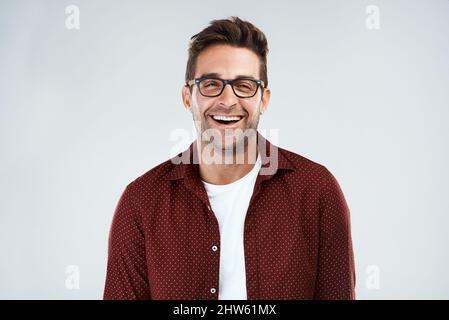 Drôle et intelligent. Portrait d'un jeune homme gai portant des lunettes et souriant de façon éclatante, debout sur un fond gris. Banque D'Images
