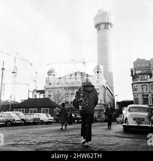 Personne marchant dans les rues de Liverpool, portant une guitare sur le dos. En arrière-plan est la tour de la ville de radio, en construction. Liverpool, Merseyside. Vers 1967. Banque D'Images