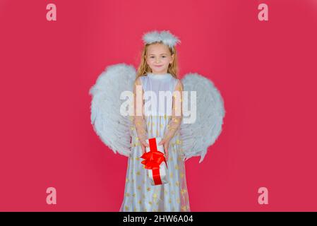 Ange pour enfants avec cadeau. Petit ange avec ailes blanches tient cadeau. Mignon ange enfant fille avec des ailes d'anges, isolé sur le rouge. Saint-Valentin Banque D'Images