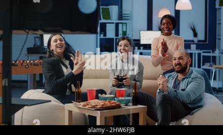 Des collègues heureux jouant à des jeux vidéo après le travail au bureau. Des collègues qui apprécient la victoire en utilisant des contrôleurs sur la console de télévision pour s'amuser avec le divertissement. Jeu gagnant Workmats Banque D'Images