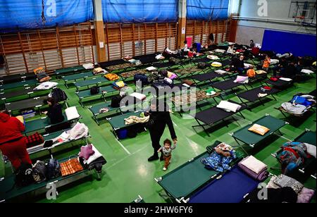 Zahony, Hongrie. 04th mars 2022. Un homme qui a fui l'Ukraine marche avec sa jeune fille à travers une salle de sport d'école transformée en refuge d'urgence à Zahony, dans le nord-est de la Hongrie, à la frontière avec l'Ukraine. La frontière entre la Hongrie et l'Ukraine fait environ 140 kilomètres de long. Les réfugiés de guerre d'Ukraine arrivent par cinq passages frontaliers routiers ainsi que par des trains arrivant à Zahony. Crédit : Marton Monus/dpa/Alay Live News Banque D'Images