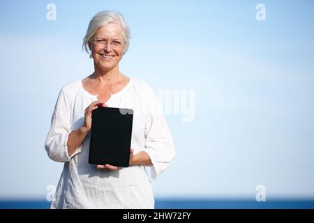 Shes a trouvé de grands exercices de relaxation en ligne. Portrait d'une femme mûre tenant une tablette numérique debout à l'extérieur. Banque D'Images