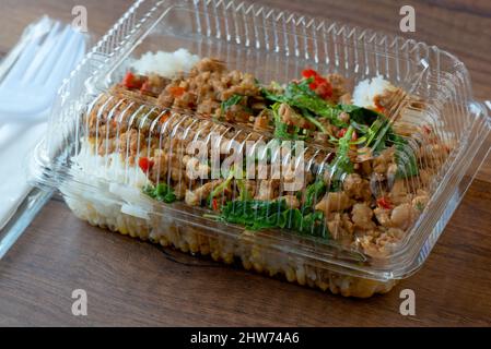 Riz frit au basilic avec porc haché dans une boîte en plastique sur fond de bois. Banque D'Images