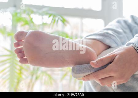 Les mains d'une femme utilisant une pierre ponce pour ramollir ses pieds après avoir enlevé des calloses. Soins du corps et podiatrie concept Banque D'Images