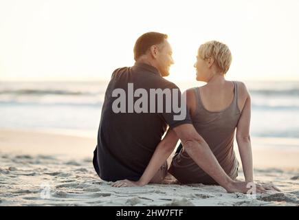 En regardant les marées se dérouler avec celui que j'aime. Un couple aimant assis sur la plage - vue arrière. Banque D'Images