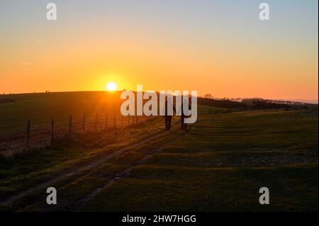 Heure d'or : un couple romantique se promenant main dans la main dans le soleil couchant le long du chemin sur South Downs Way près de Ditchling Beacon à Sussex, Angleterre. Banque D'Images