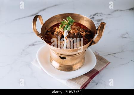 Curry de bœuf Massaman traditionnel dans un plat de ragoût de cuivre isolé sur le dessus du tapis vue sur fond de marbre gris Banque D'Images