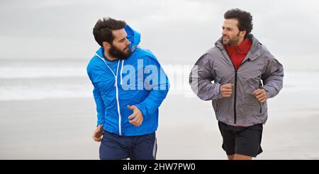 Courir le matin sur la plage. Plan court de deux jeunes hommes qui font du jogging ensemble le long de la plage un matin couvert. Banque D'Images