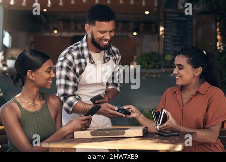 Ne vous inquiétez pas, j'ai eu celui-ci. Prise de vue de deux jeunes femmes assises dans un restaurant et utilisant une machine à carte de crédit pour payer leur repas. Banque D'Images