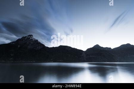 Le soir, nuages au-dessus des montagnes. Exposition longue. Le ciel est dans la couleur de l'après-coucher du soleil. Réflexions à la surface du lac. Banque D'Images