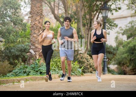 Les jeunes font du sport au parc. Ils sont en train de courir et de sourire Banque D'Images