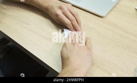 Main d'un homme pliant une feuille de papier pour faire un plan. Concept d'activités créatives, gros plan des mains masculines faisant de l'origami sur une table en bois. Banque D'Images