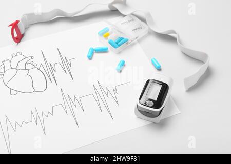 Oxymètre de pouls, cardiogramme et pilules sur fond blanc, gros plan Banque D'Images