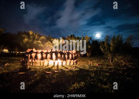 Une belle photo de personnes dansant autour d'un feu de camp, sous le clair de lune, dans une forêt tropicale Banque D'Images