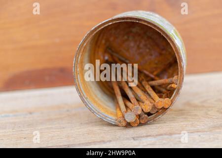 Quelques ongles rouillés dans un rouillé peut sur un fond en bois. Banque D'Images