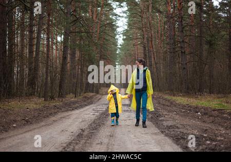 Maman et enfant marchant le long de la route forestière après la pluie en imperméable ensemble Banque D'Images