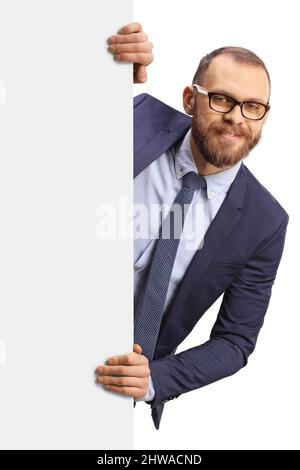 Jeune homme avec des lunettes qui se cachent derrière un panneau blanc vierge isolé sur fond blanc Banque D'Images