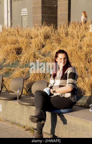 jeune femme se posant assise sur un banc, avec une chemise à carreaux et des cheveux rougeâtres Banque D'Images