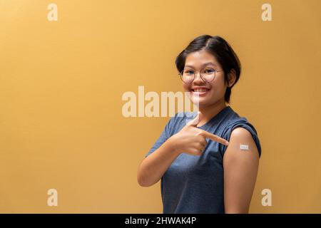 Asian Happy girl index du doigt à l'épaule et montrant son bras avec bandage après avoir été vacciné, immunisation des adolescents, vaccin préventif Covid. Banque D'Images