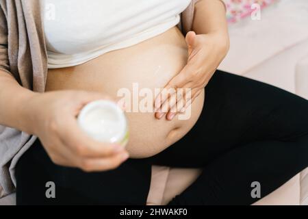 Un concept de grossesse, de personnes et de maternité - gros plan de la femme enceinte appliquant une crème de marque extensible au ventre Banque D'Images