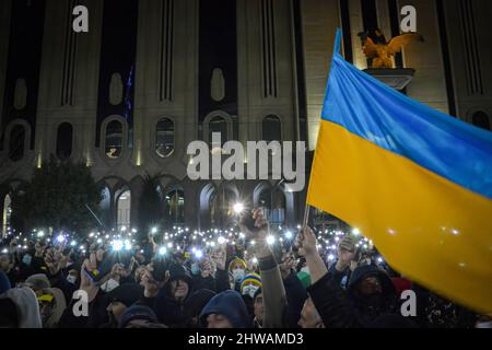 Tbilissi, Géorgie. 04th mars 2022. Une foule de gens tient la lumière de leur téléphone mobile et un drapeau ukrainien est brandi alors que les gens attendent le discours du président Volodymyr Zelenskyy. Trente mille personnes se sont rassemblées devant le bâtiment du Parlement de Tbilissi pour écouter le discours en direct du président de l'Ukraine où il déclare que « l'Ukraine ne donnera jamais son territoire à la Russie et l'Ukraine se battra contre les Russes pour gagner cette guerre. Vous êtes tous des Ukrainiens aujourd'hui". Crédit : SOPA Images Limited/Alamy Live News Banque D'Images