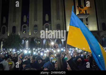 Tbilissi, Géorgie. 04th mars 2022. Une foule de gens tient la lumière de leur téléphone mobile et un drapeau ukrainien est brandi alors que les gens attendent le discours du président Volodymyr Zelenskyy. Trente mille personnes se sont rassemblées devant le bâtiment du Parlement de Tbilissi pour écouter le discours en direct du président de l'Ukraine où il déclare que « l'Ukraine ne donnera jamais son territoire à la Russie et l'Ukraine se battra contre les Russes pour gagner cette guerre. Vous êtes tous des Ukrainiens aujourd'hui". Crédit : SOPA Images Limited/Alamy Live News Banque D'Images