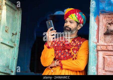 Un homme adulte originaire du nord de l'Inde, vêtu d'une tenue colorée et d'un turban avec un smartphone, souriant, appelant un homme traditionnel sur un smartphone android. Banque D'Images