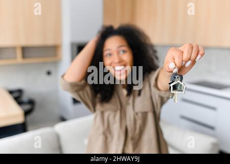 Joyeuse femme multiraciale tenant des clés avec trinket en forme de petite maison mignonne et du montrer à l'appareil photo, sélectif foyer sur les touches Banque D'Images