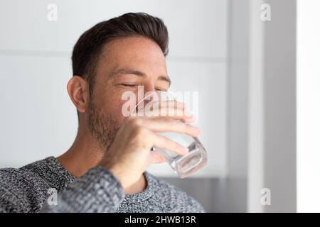 L'homme boit l'eau du verre à l'intérieur, les yeux fermés Banque D'Images