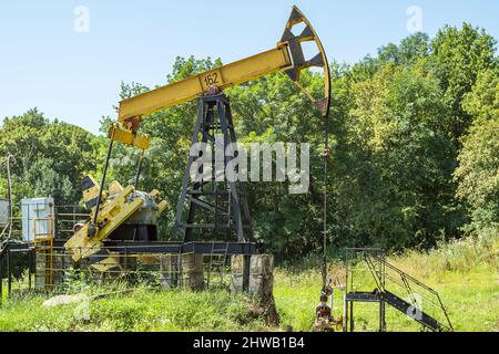 Un ancien engin de forage à huile jaune pompant de l'huile dans un défrichement dans les bois. En arrière-plan sont des arbres et un ciel bleu. Extraction de l'or noir du puits Banque D'Images